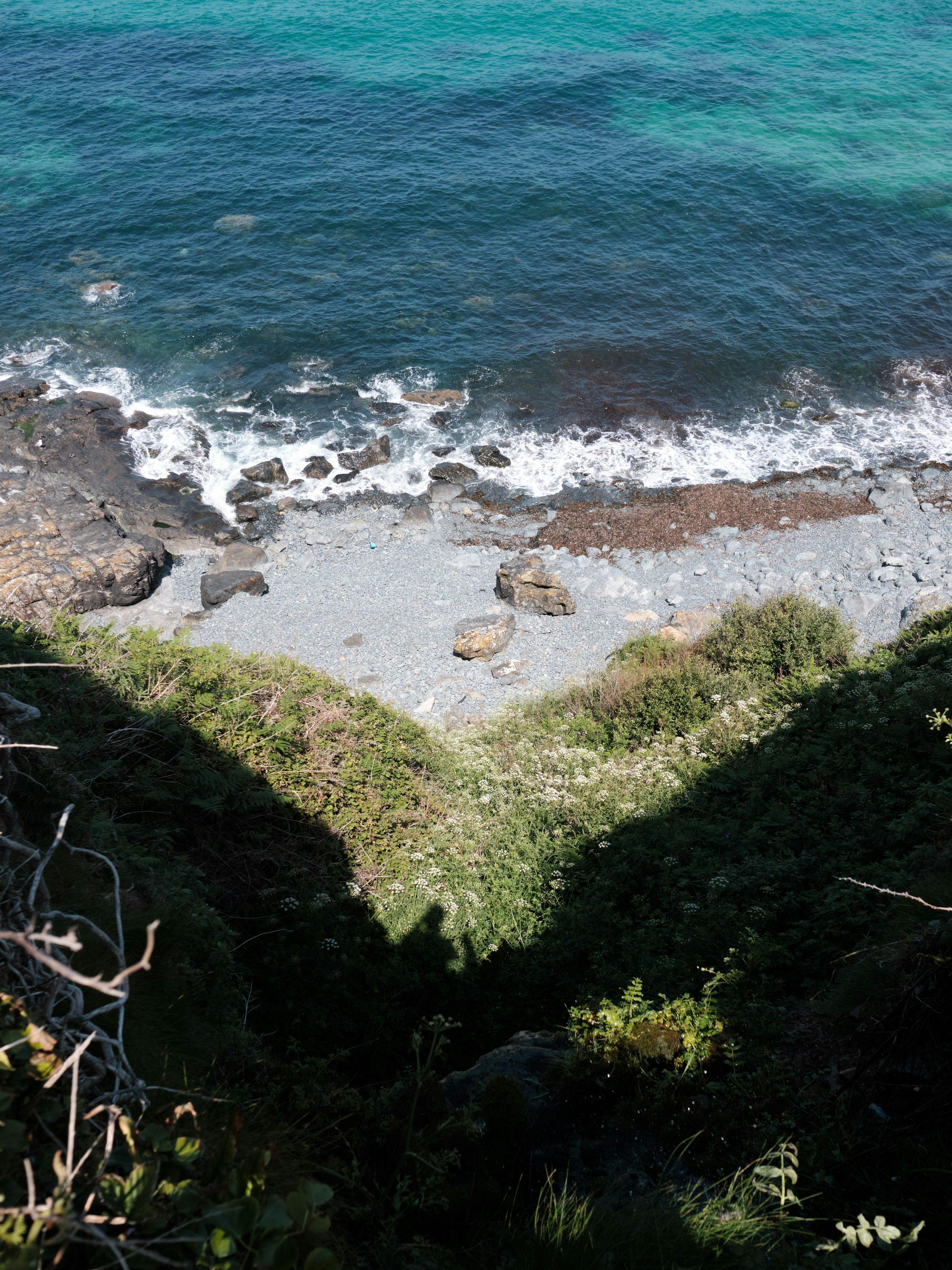 The shadow of the cliff forms a whale tale on the grass and pebbles of the beach below.