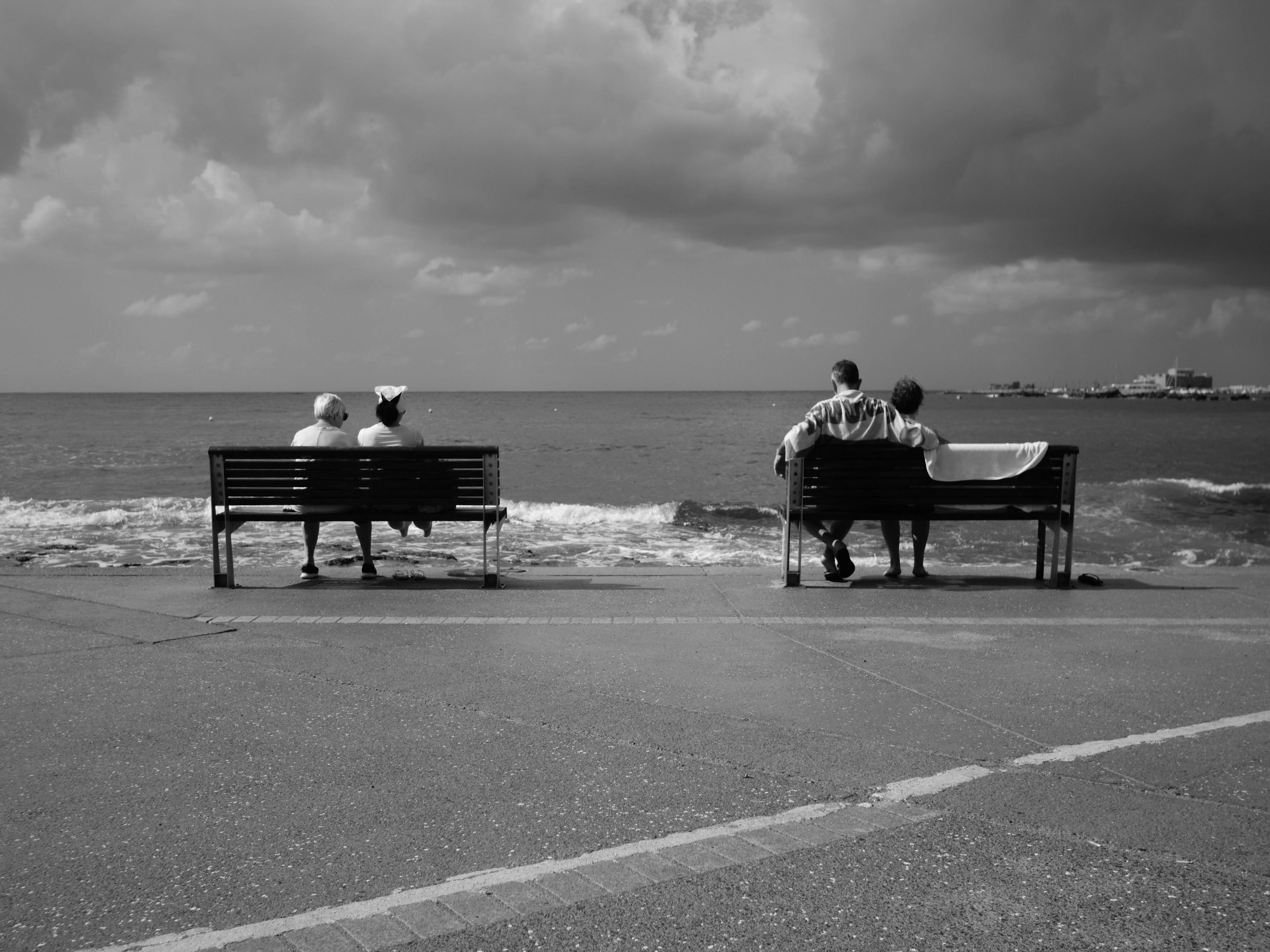 Two sets of couples on respective benches looking out to sea