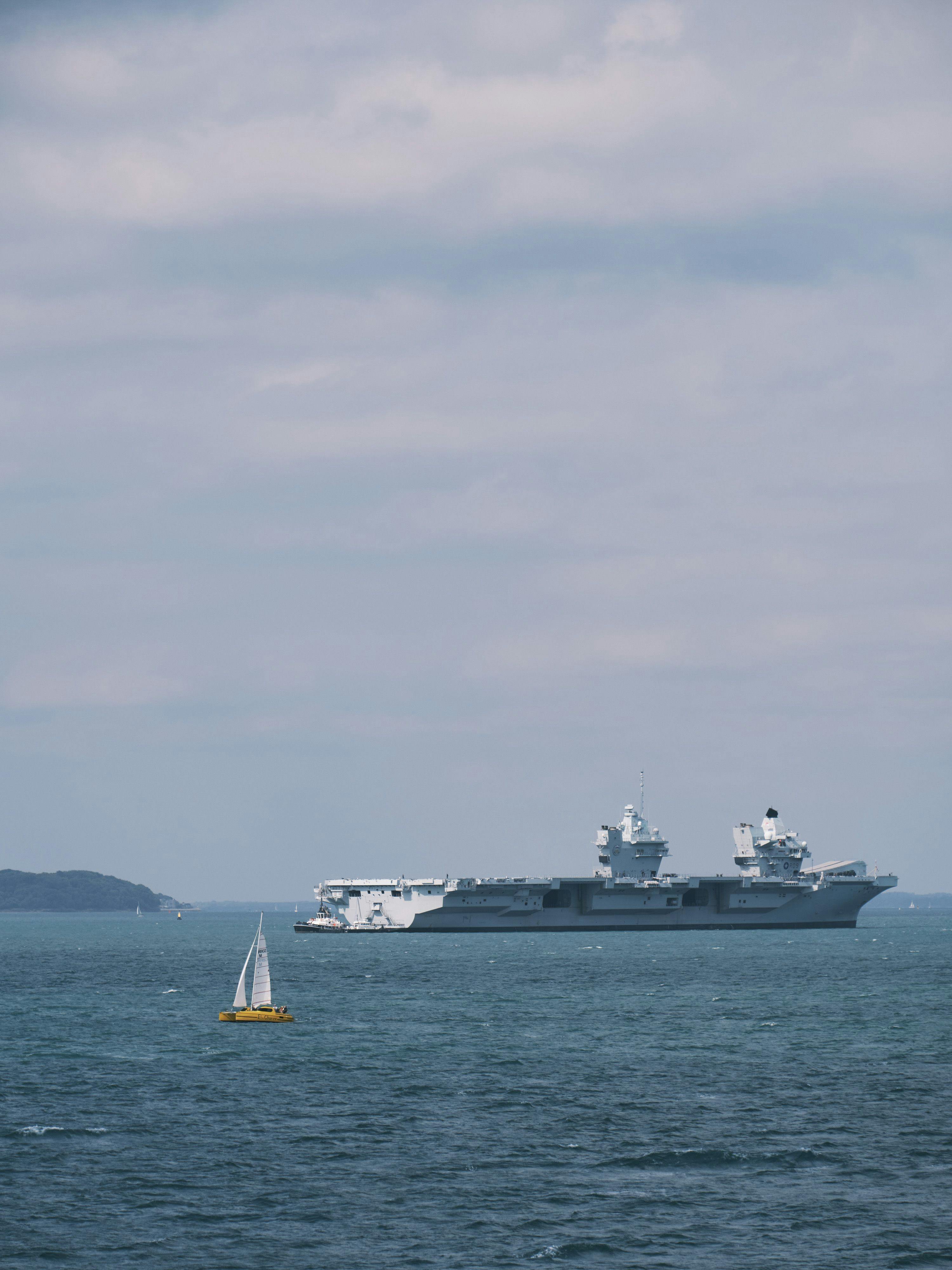 A small sail boat sails past an aircraft carrier