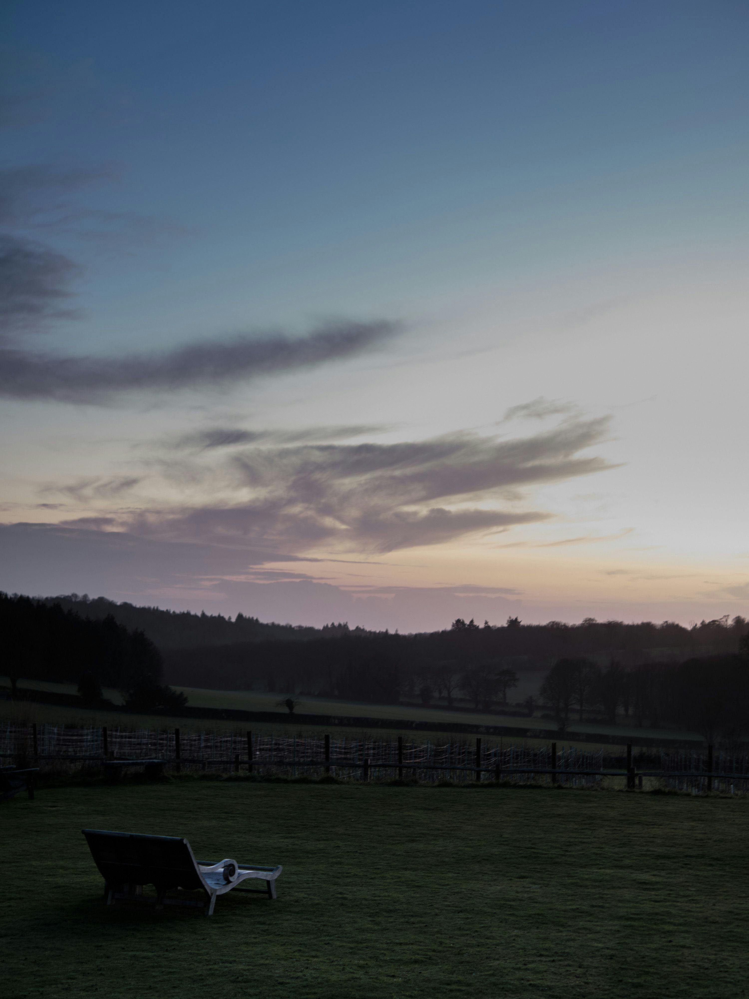 A reclined deck chair looks out to the vineyards at the blue hour.
