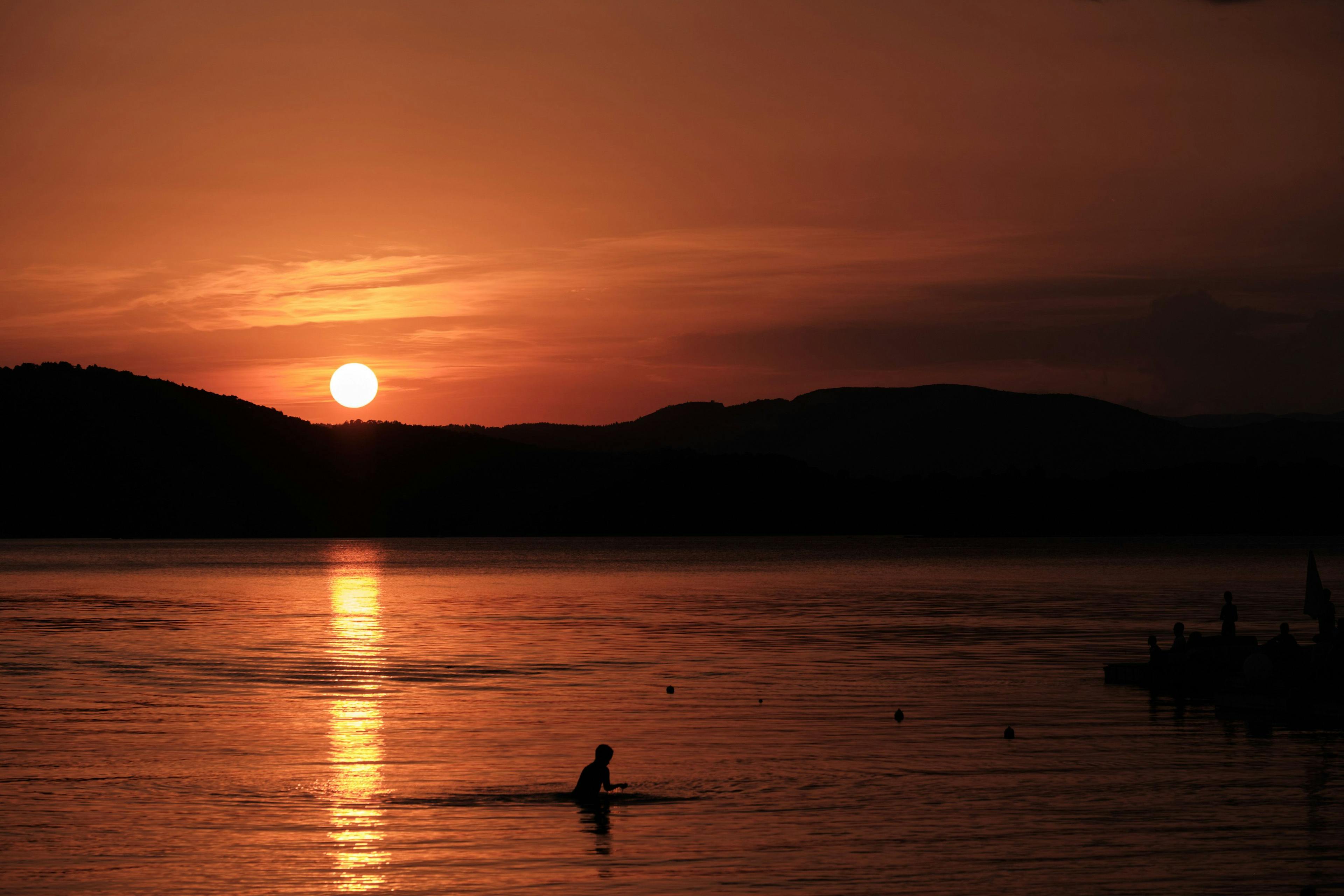 A sunset that has turned the sky and sea orange. A lone figure plays in the water.