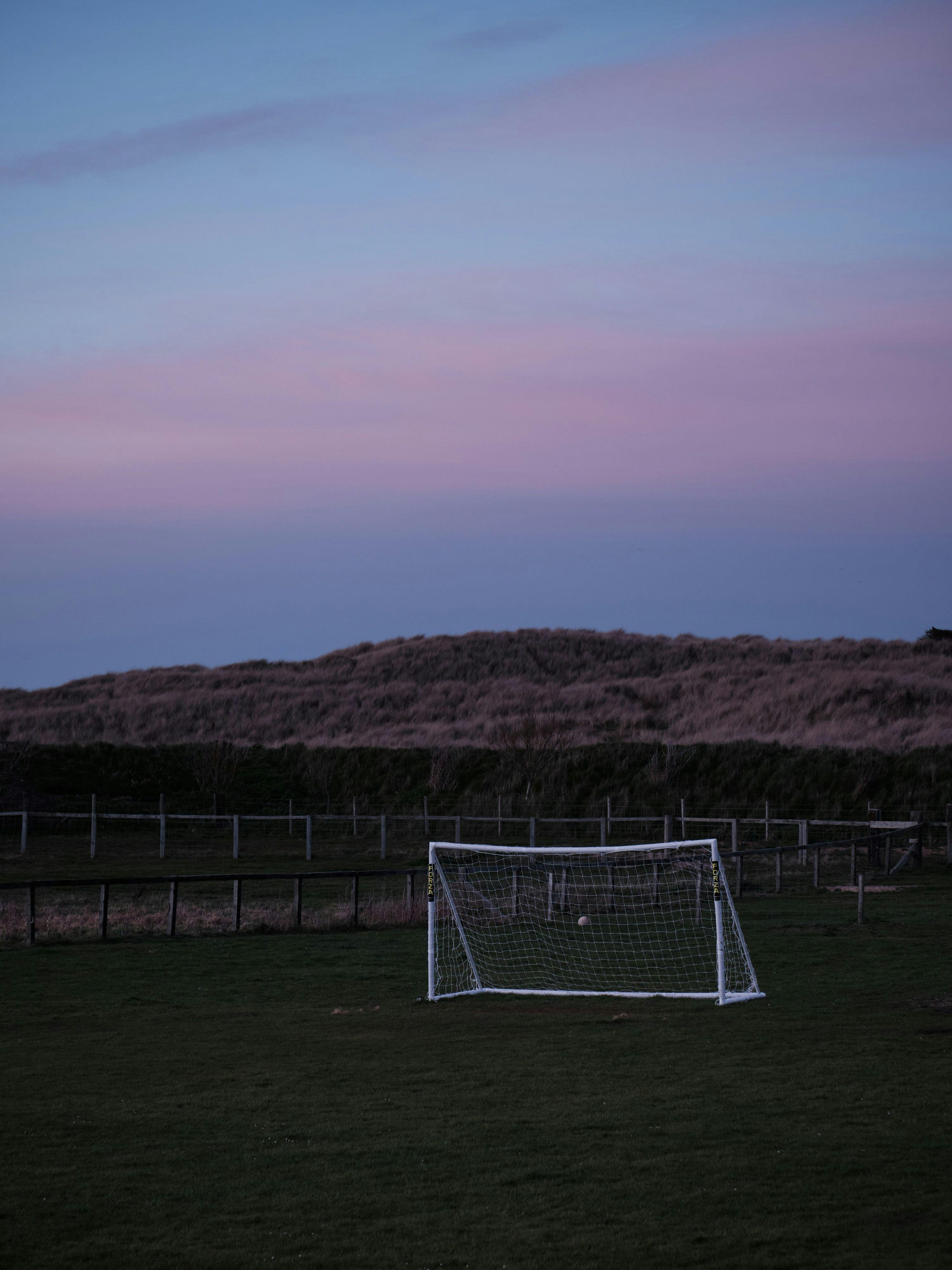 A football net in a field against the dunes, the sky has gone pink and blue as the light goes.